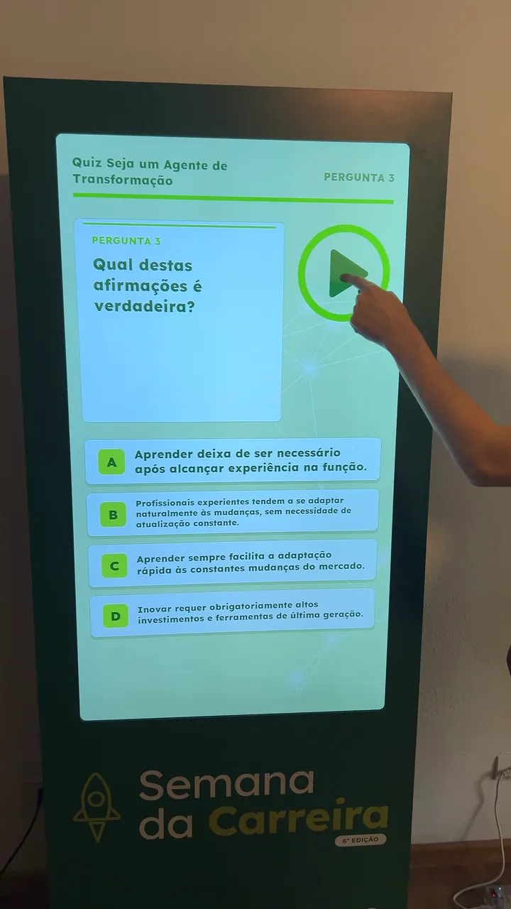 Mão toca a tela do totem do quiz “Seja um Agente de Transformação” da Semana da Carreira