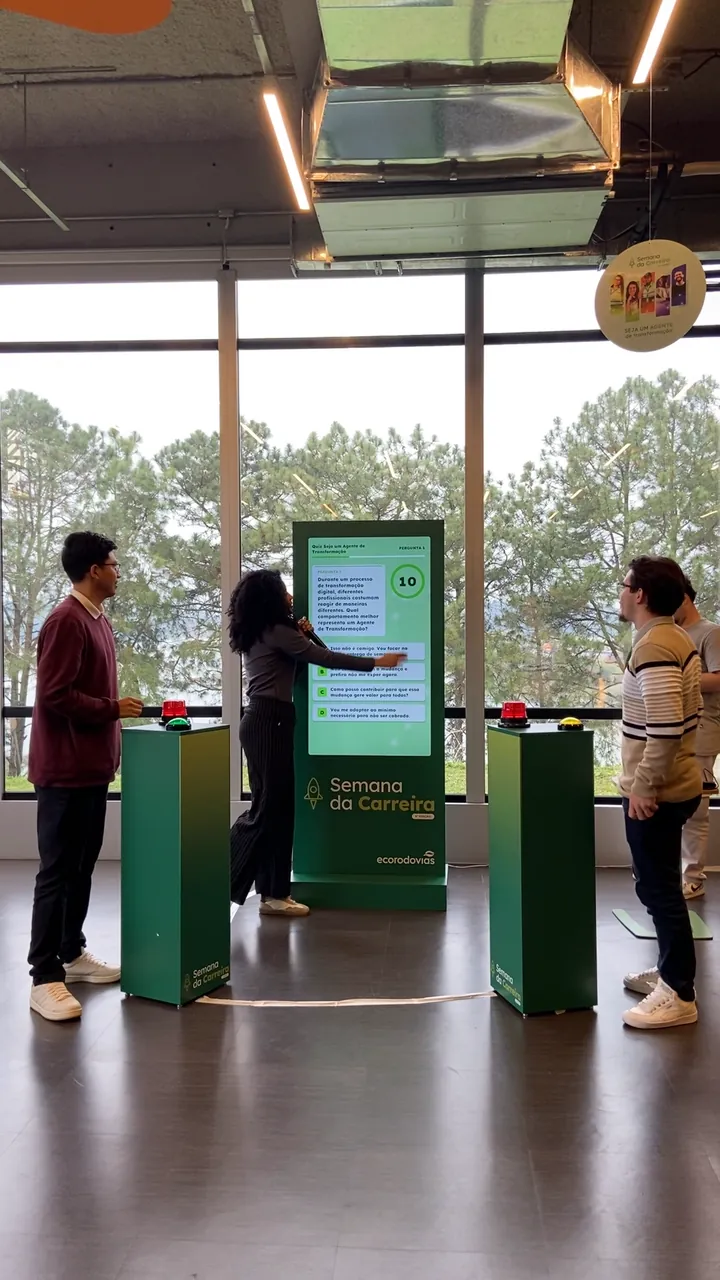 Dois colaboradores em duelo nos botões do quiz, diante do totem da Semana da Carreira